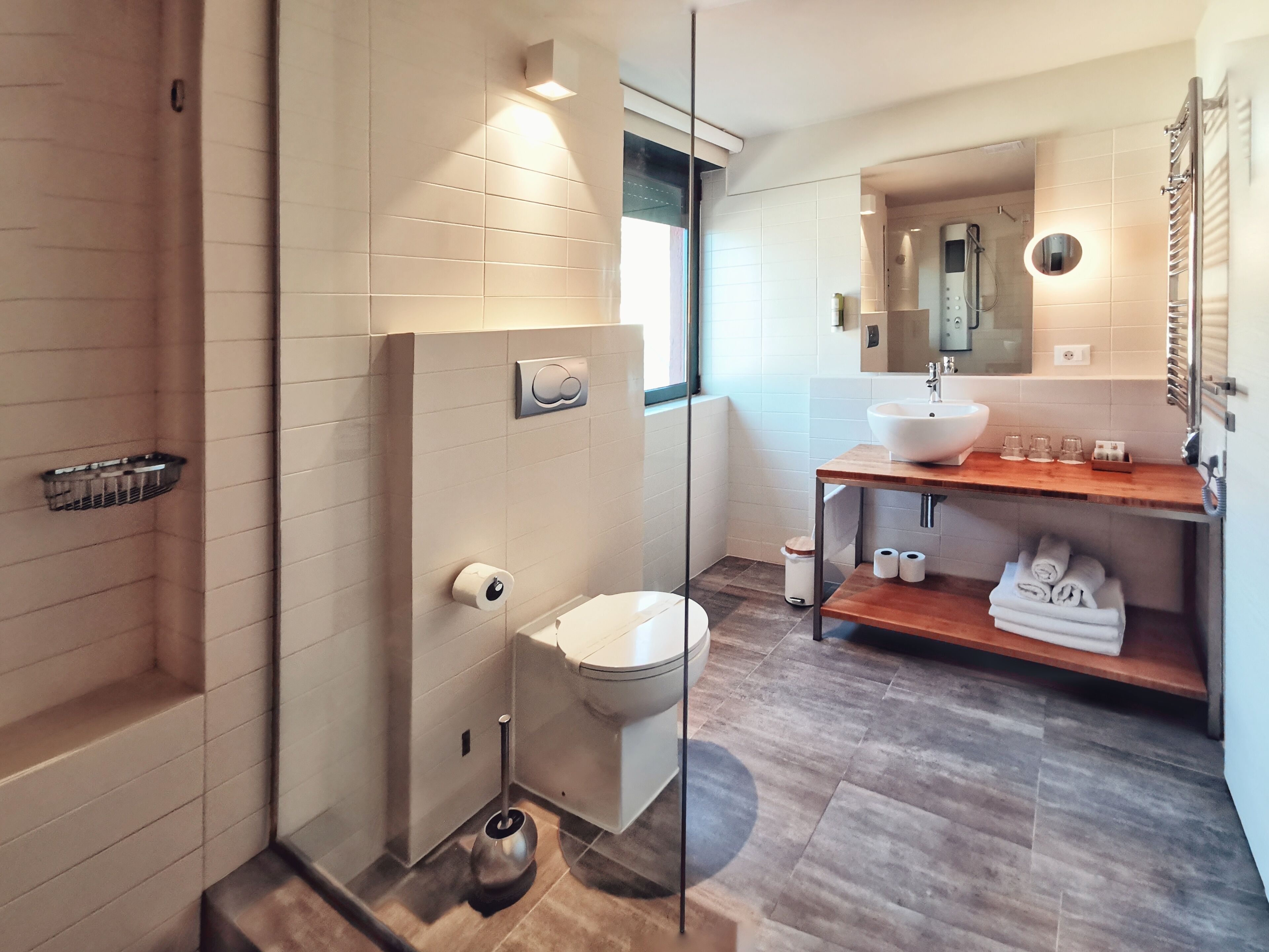 Un baño moderno con mampara de vidrio, inodoro, bidé, lavamanos con encimera de madera y un perchero para toallas.