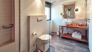 Un baño moderno con mampara de vidrio, inodoro, bidé, lavamanos con encimera de madera y un perchero para toallas.