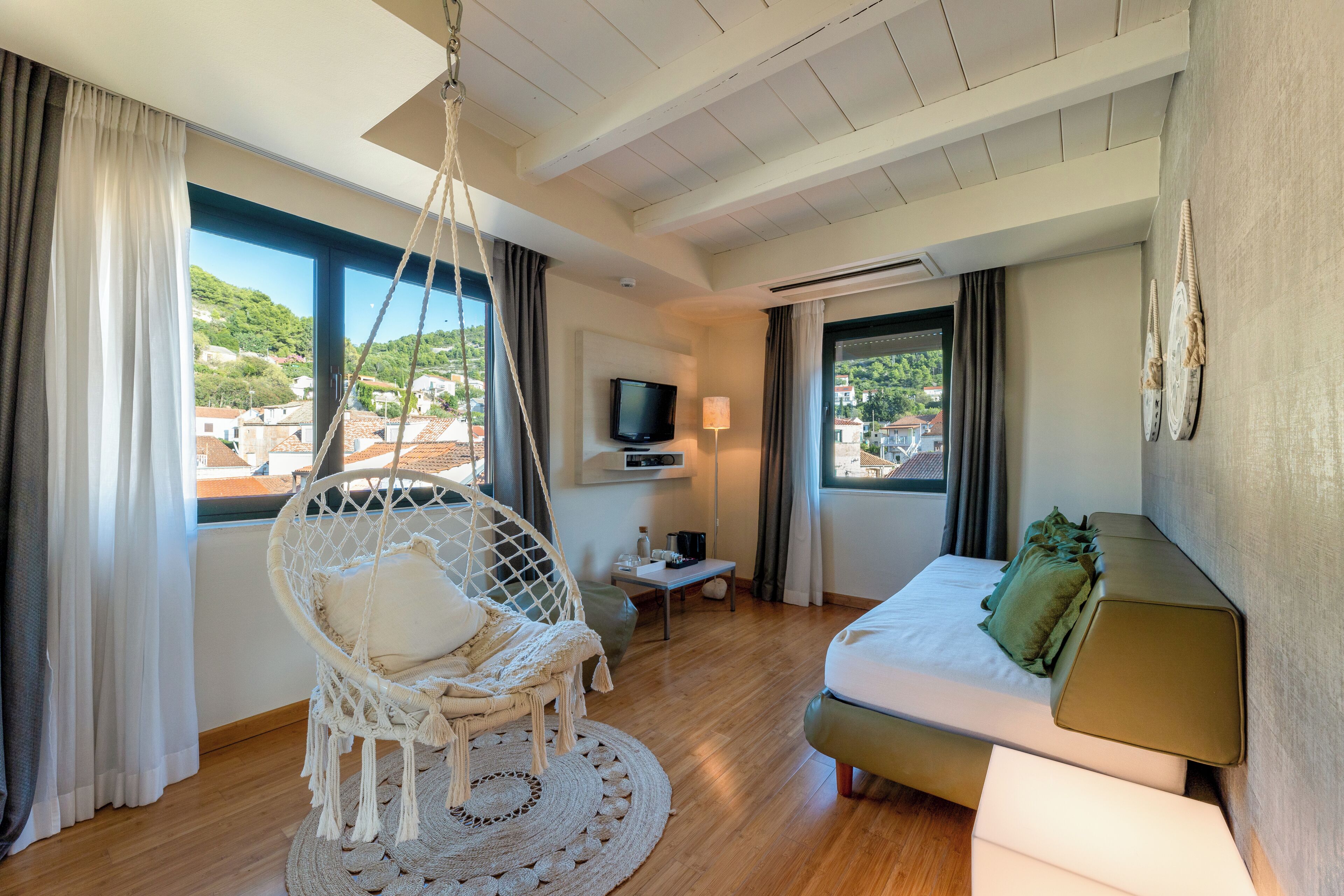 A modern hotel room with a hanging chair, a sofa, a TV, and a view of the city.
