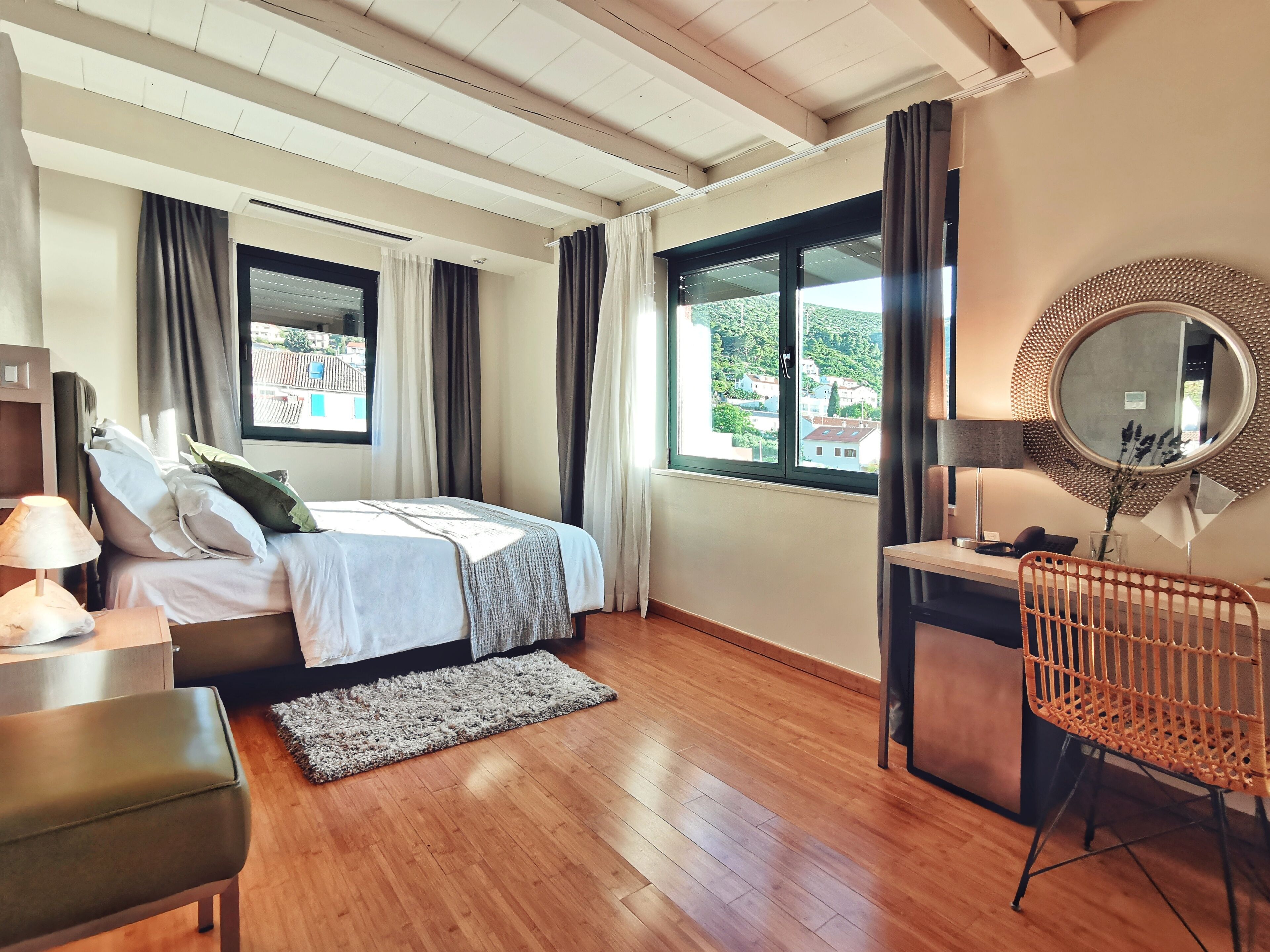 Een slaapkamer met een bed, nachtkastje, lamp, stoel en uitzicht op buiten door grote ramen.