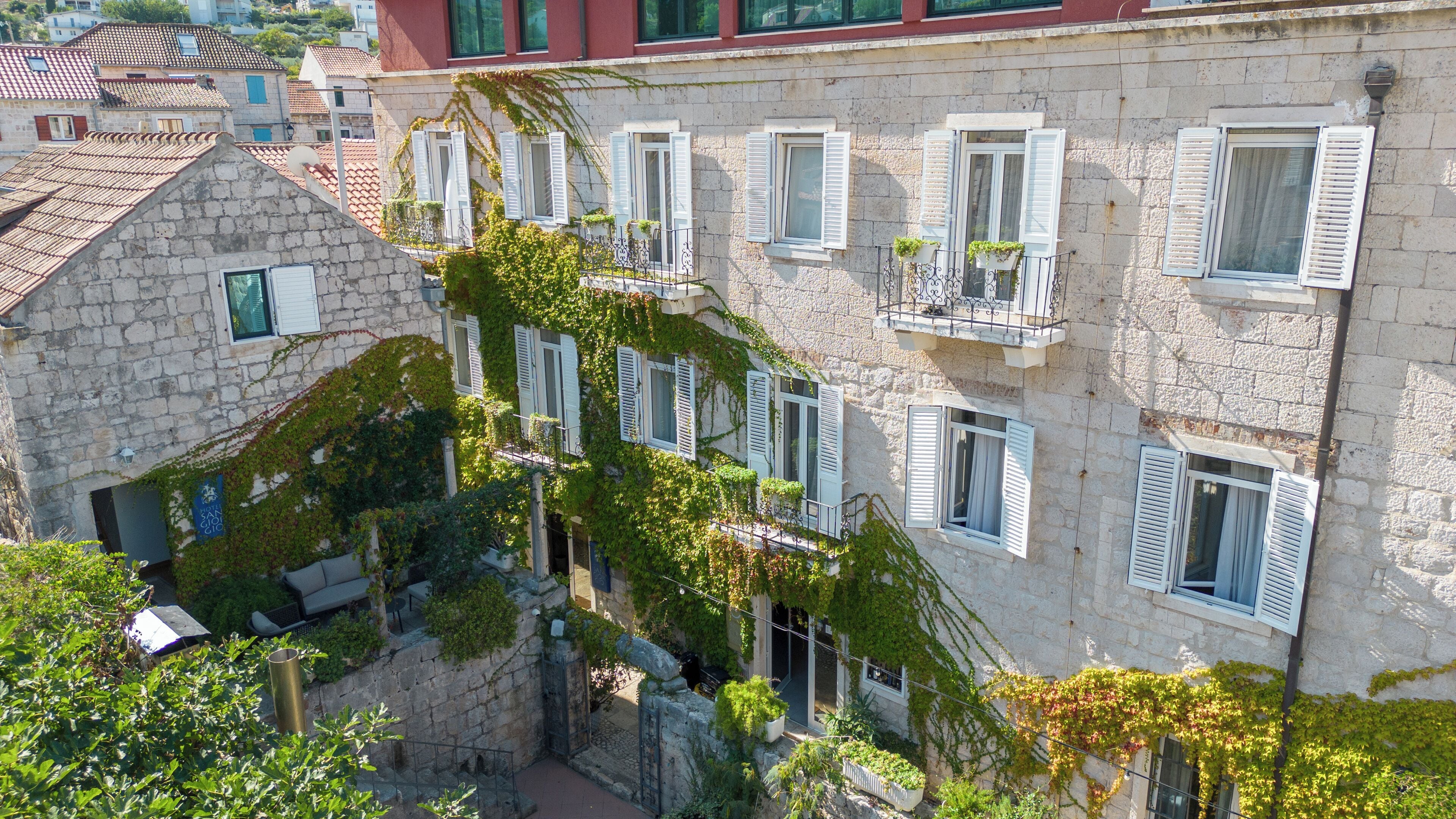 A stone building with multiple windows, some with shutters, and a balcony with potted plants.