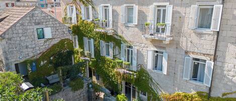 A stone building with multiple windows, some with shutters, and a balcony with potted plants.