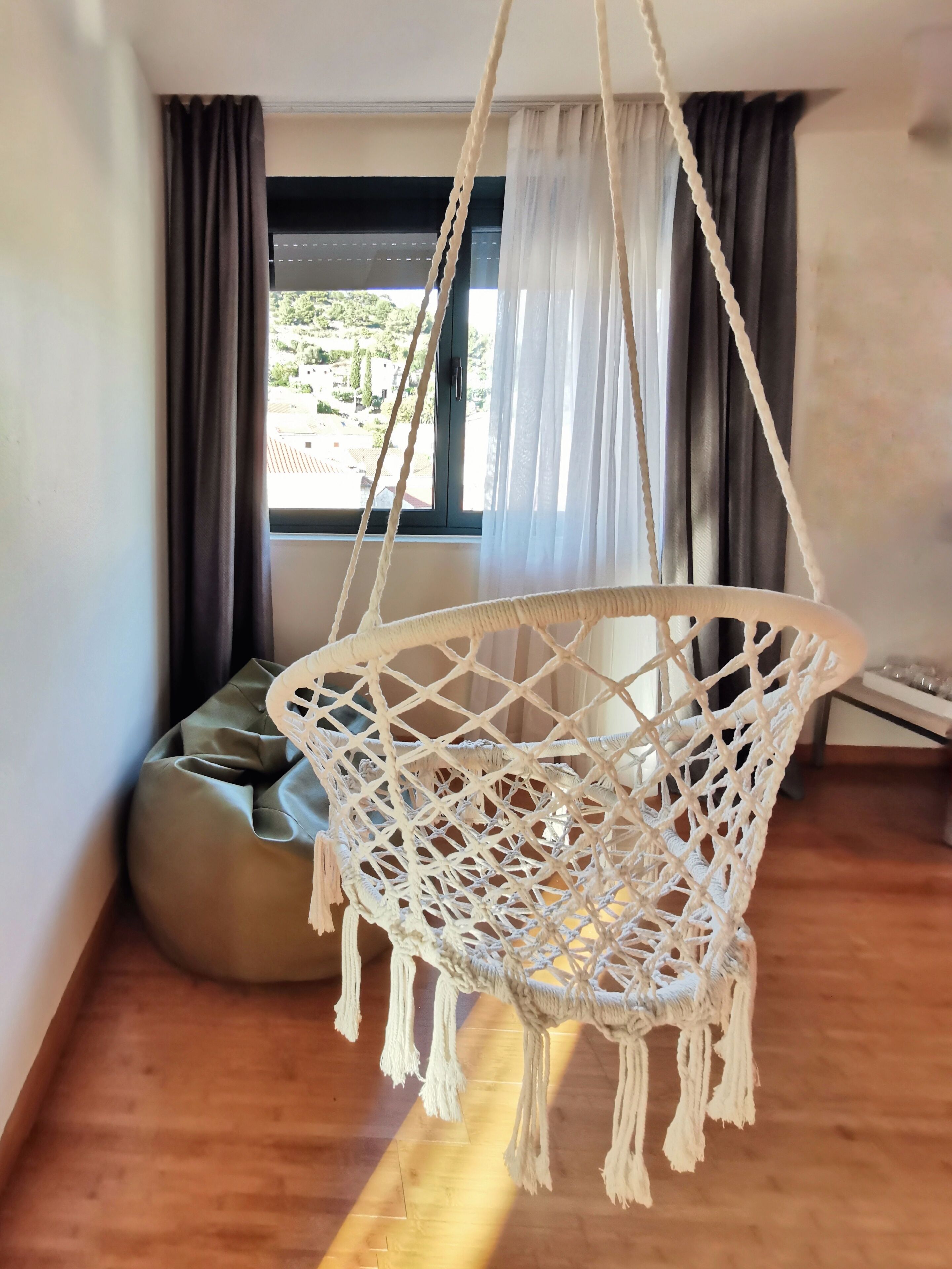 Una habitación con una hamaca de macramé, un sillón de tierno y vistas a la vegetación.