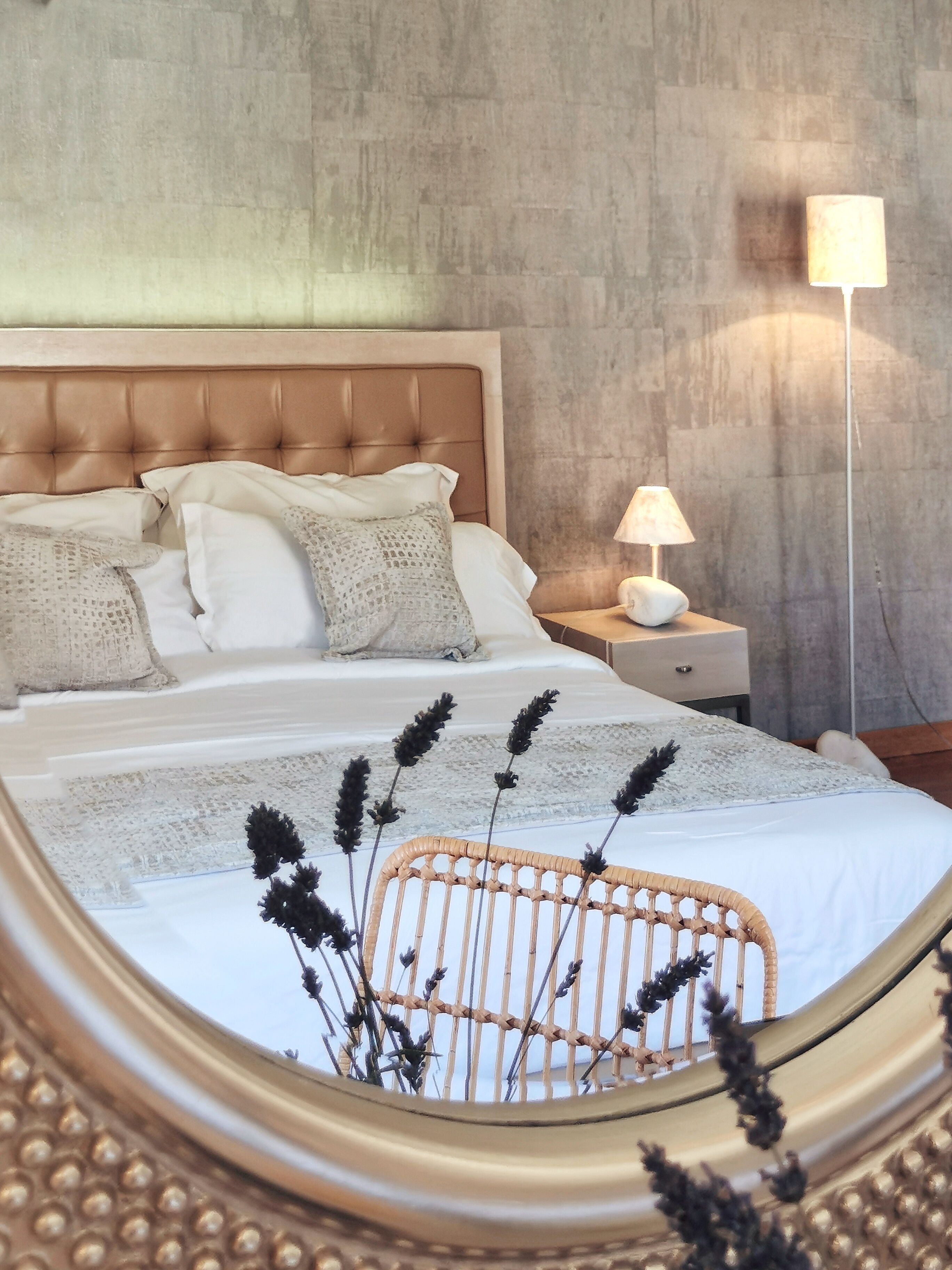A bedroom with a tufted headboard, a bedside table with a lamp, and a wicker chair.