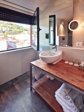 A modern bathroom with a large window, a white sink, and a wooden vanity.