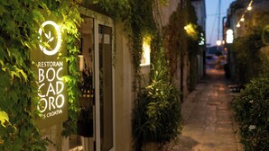 Um beco estreito com o letreiro de um restaurante, cercado por vegetação e paredes de pedra.