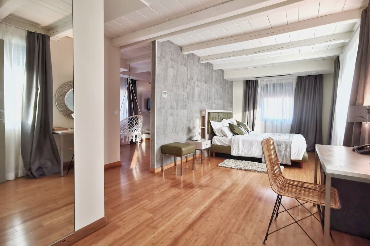 Un dormitorio moderno con una cama grande, un escritorio y una silla. La habitación tiene suelo de madera y una pared de acento de piedra.