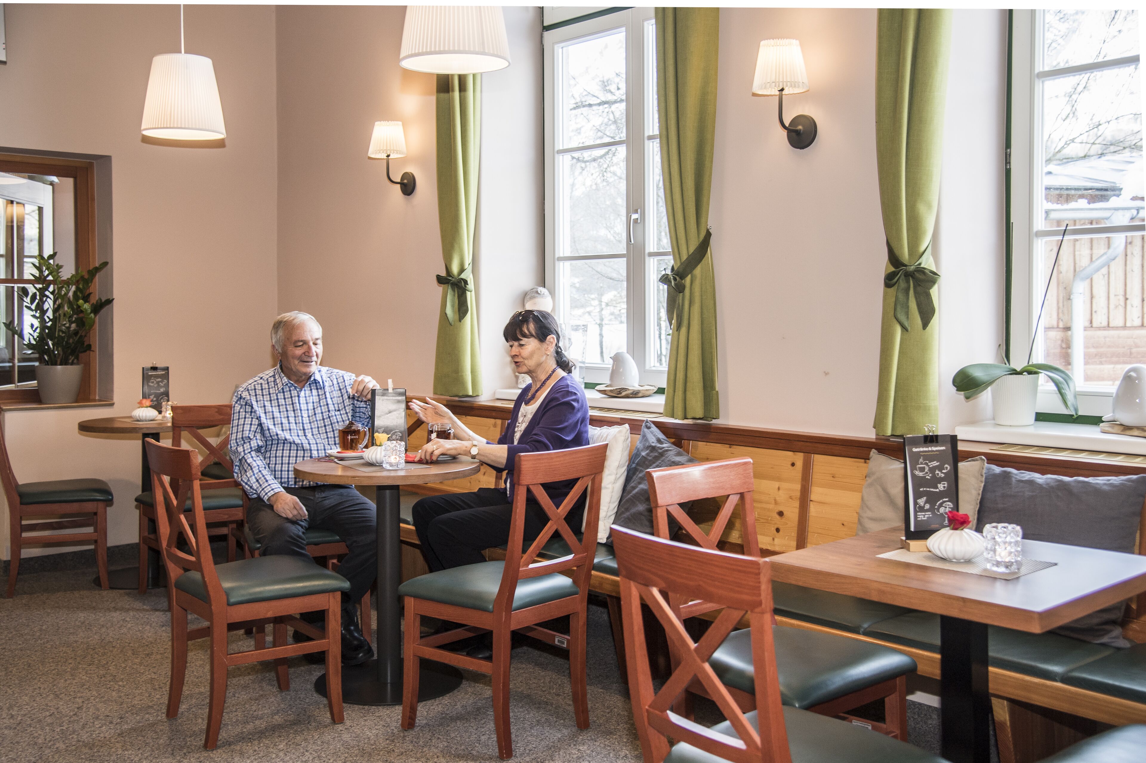 A cozy dining area with wooden furniture, green curtains, and pendant lighting.