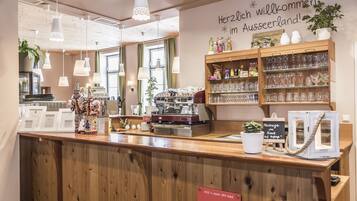 Zona de recepción de hotel con mostrador de madera, una máquina de café y un cartel de bienvenida a los huéspedes.
