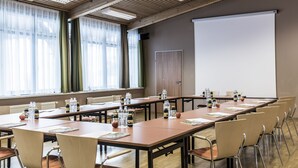 Een vergaderruimte met een lange tafel, stoelen, een projectiescherm en ramen voorzien van gordijnen.