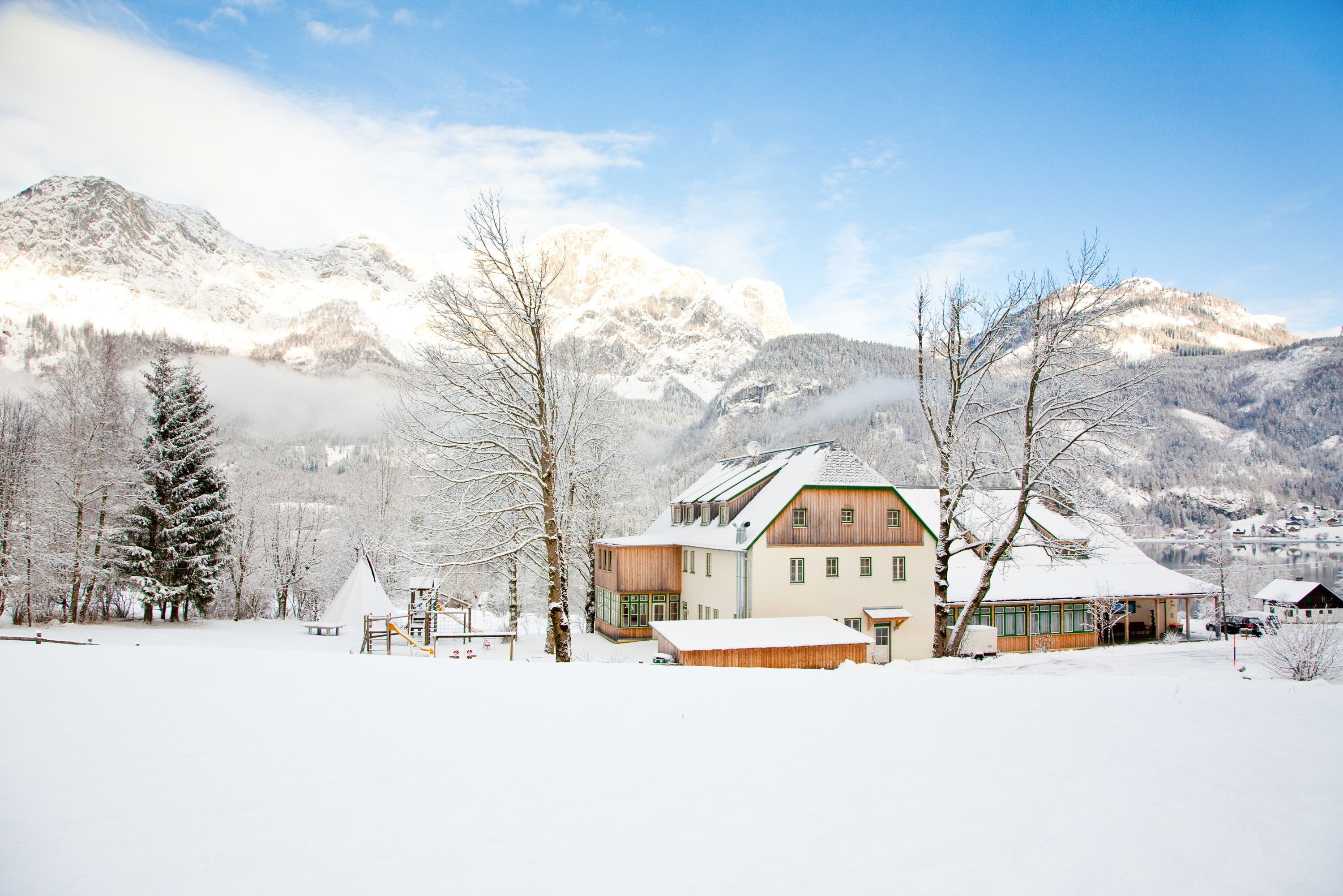 A snow-covered mountain landscape with a wooden house featuring a sloped roof and large windows.