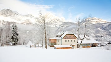 A snow-covered mountain landscape with a wooden house featuring a sloped roof and large windows.