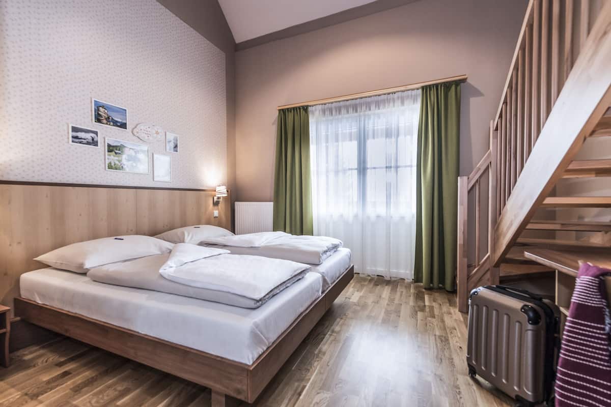 Habitación de hotel con una cama de madera, una maleta, un radiador y una escalera.