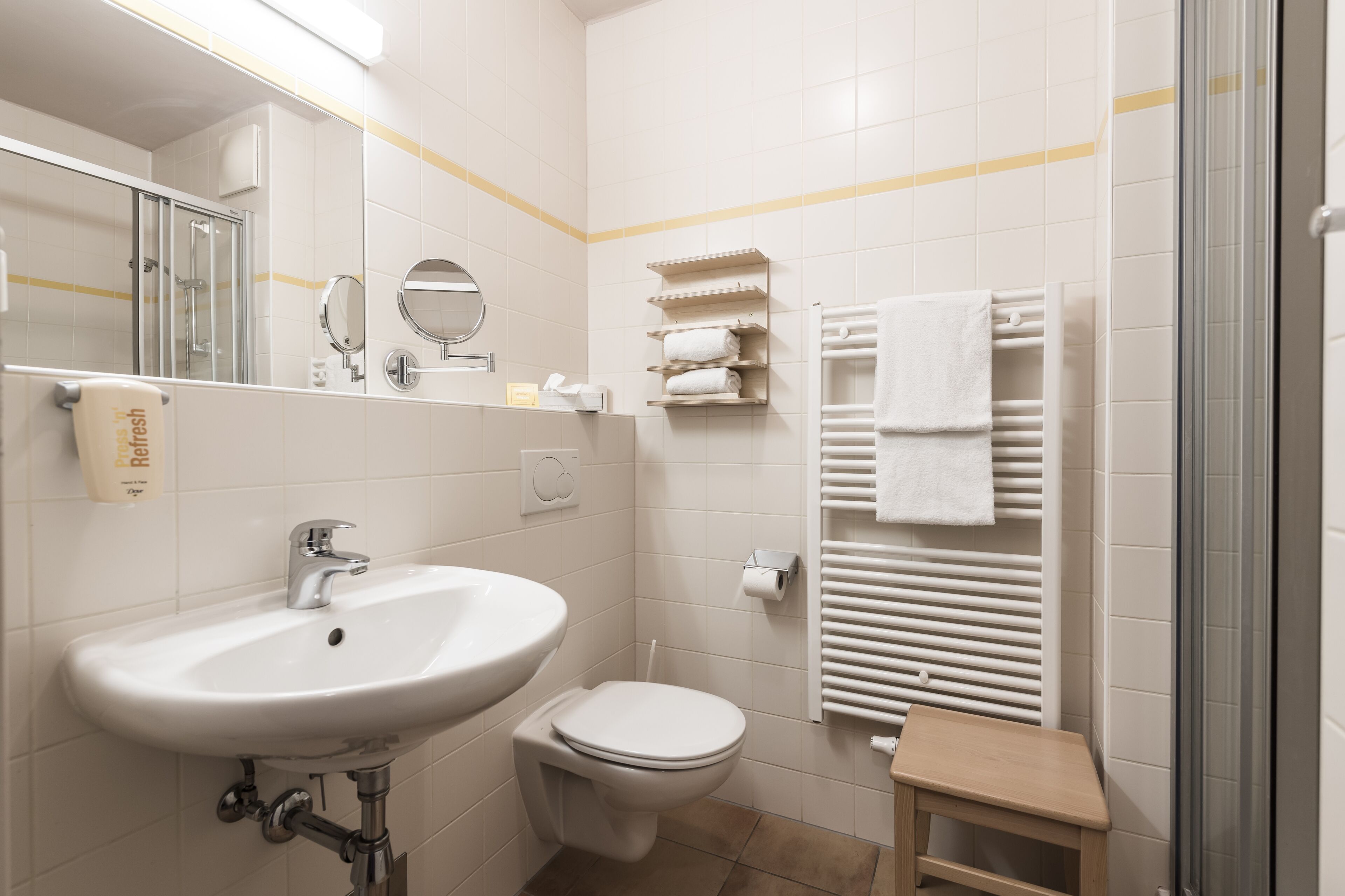 A bathroom with a sink, toilet, mirror, towel rack, and a small wooden stool.