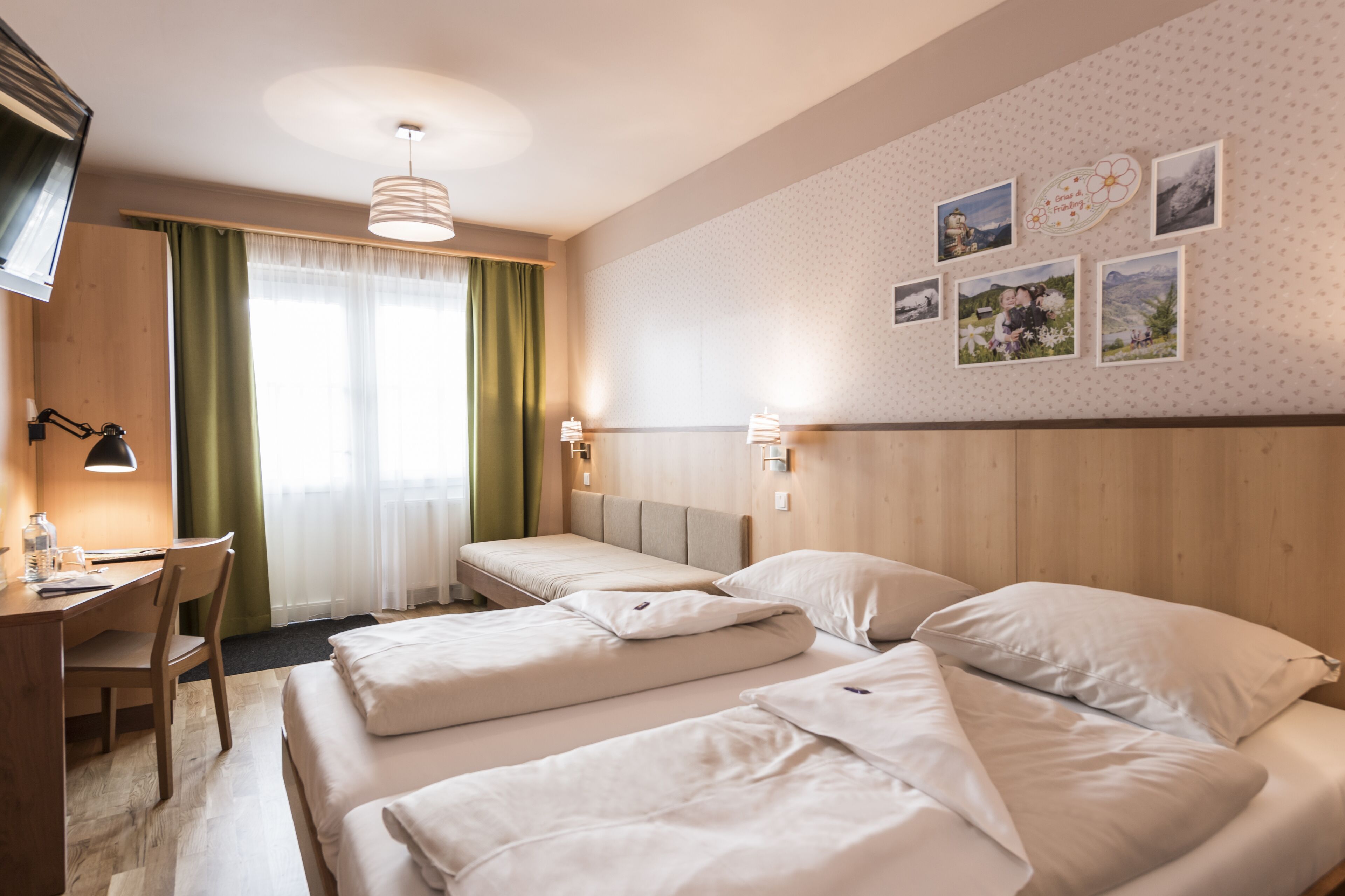 A hotel room with two beds, a desk, and a chair. There are wall-mounted lamps and a ceiling light.