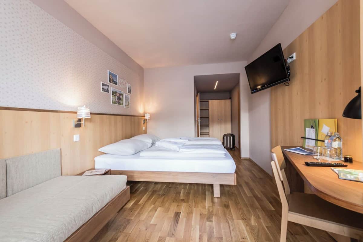 Habitación de hotel con cama, escritorio, silla, televisor y armario.