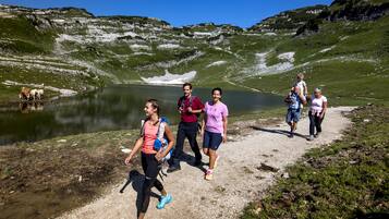 Un grupo de personas caminando por un sendero junto a un lago, con montañas al fondo.