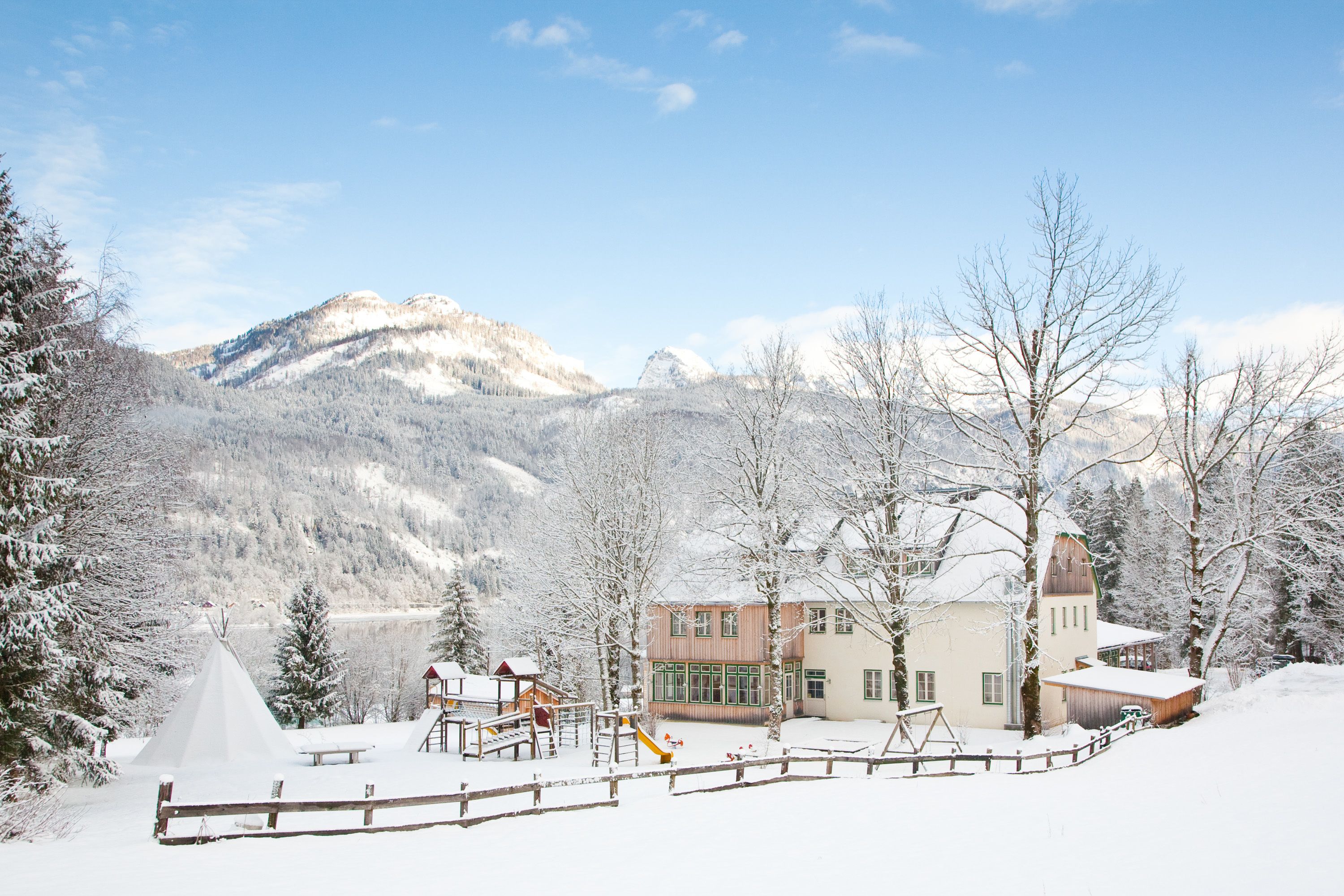 A snow-covered lodge with a play area, a large building with a tower, and mountains in the background.