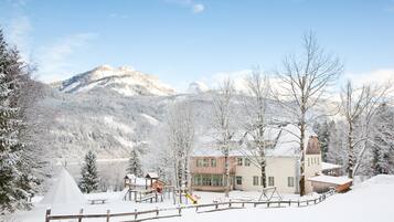 A snow-covered lodge with a play area, a large building with a tower, and mountains in the background.