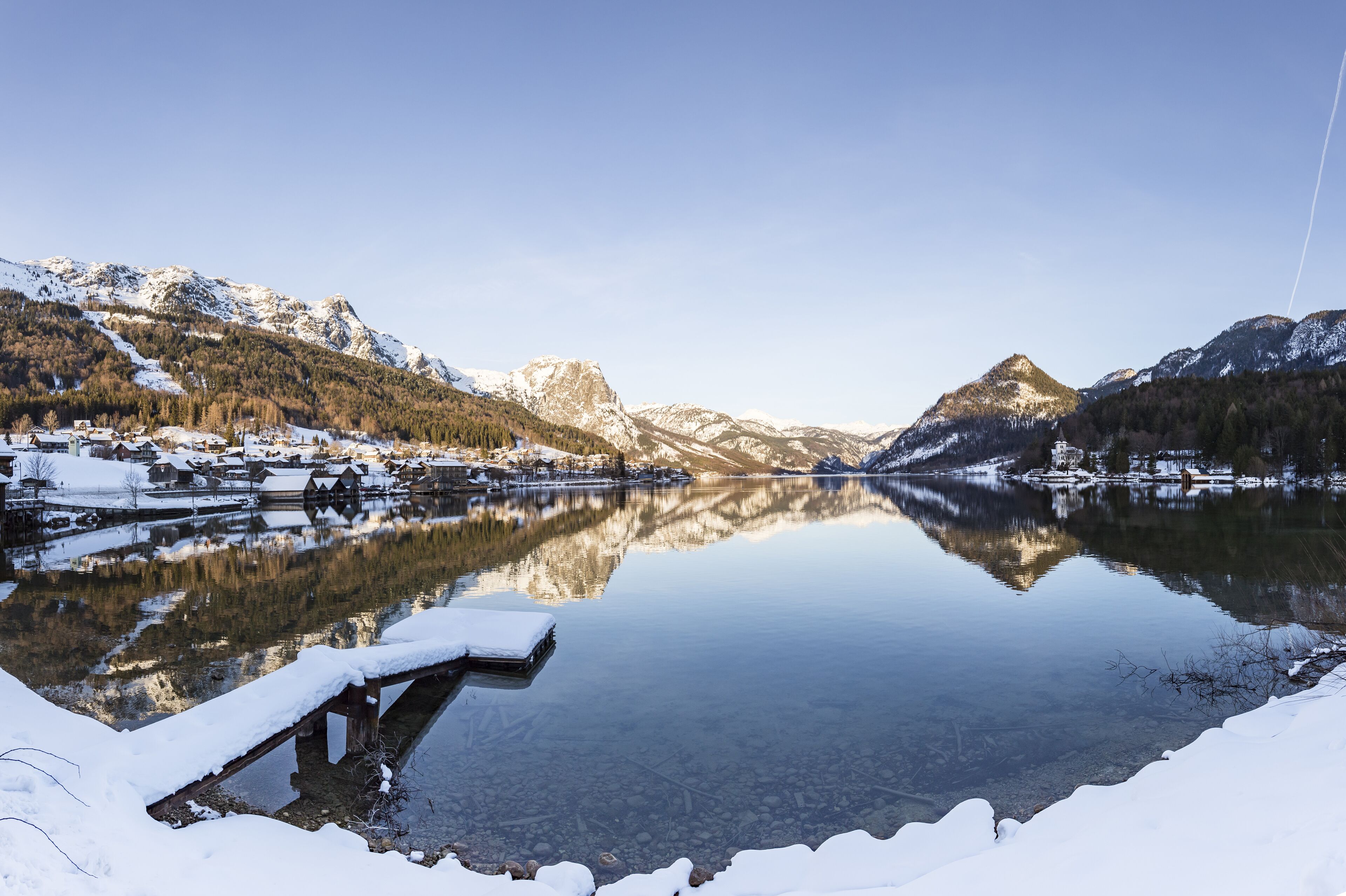 A serene winter landscape with a clear lake reflecting the surrounding mountains and a small dock.