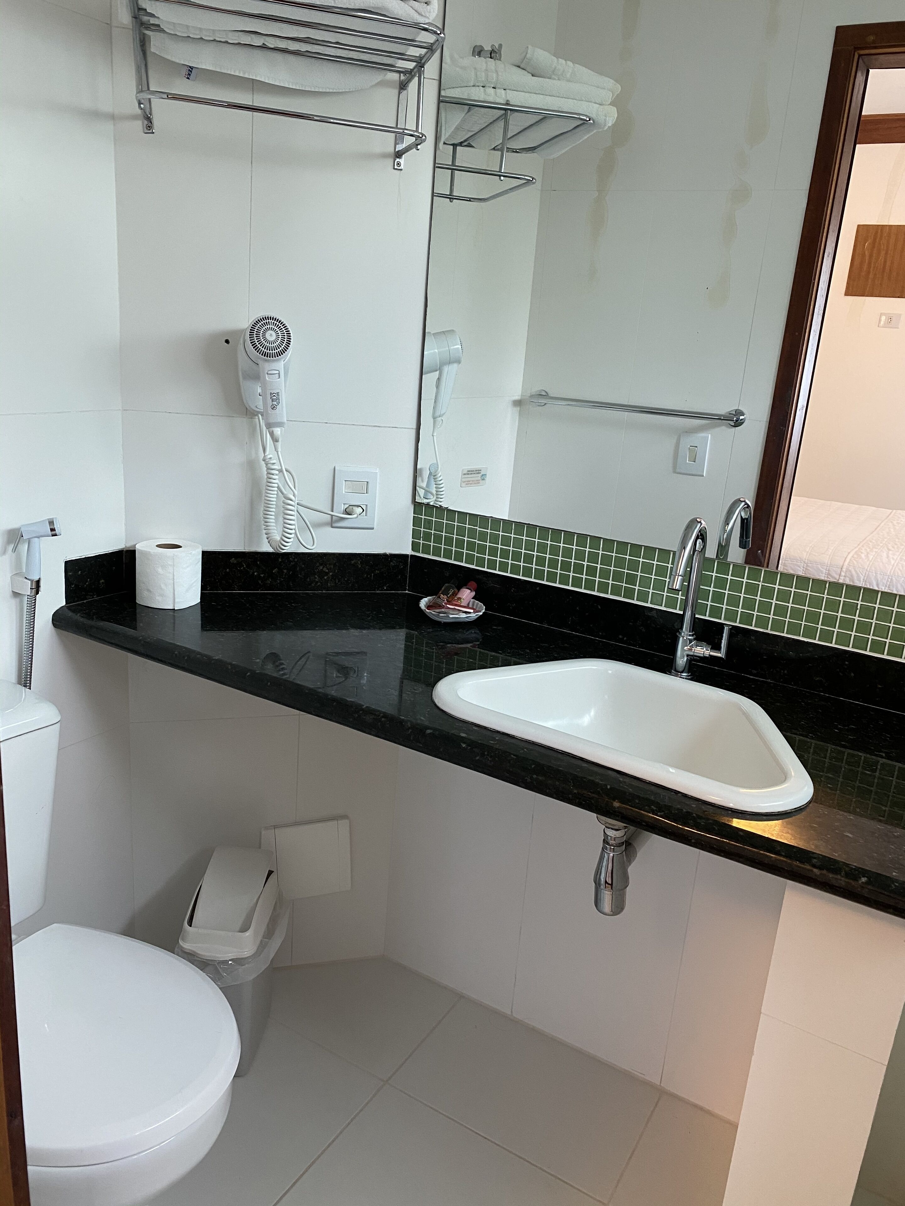Une salle de bain avec des toilettes blanches, un lavabo doté d’un plan-vasque noir, un sèche-cheveux et un porte-serviettes.