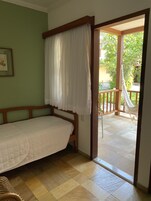 Een slaapkamer met een houten bed, een witte hemelbed en uitzicht op een balkon met een hangmat.