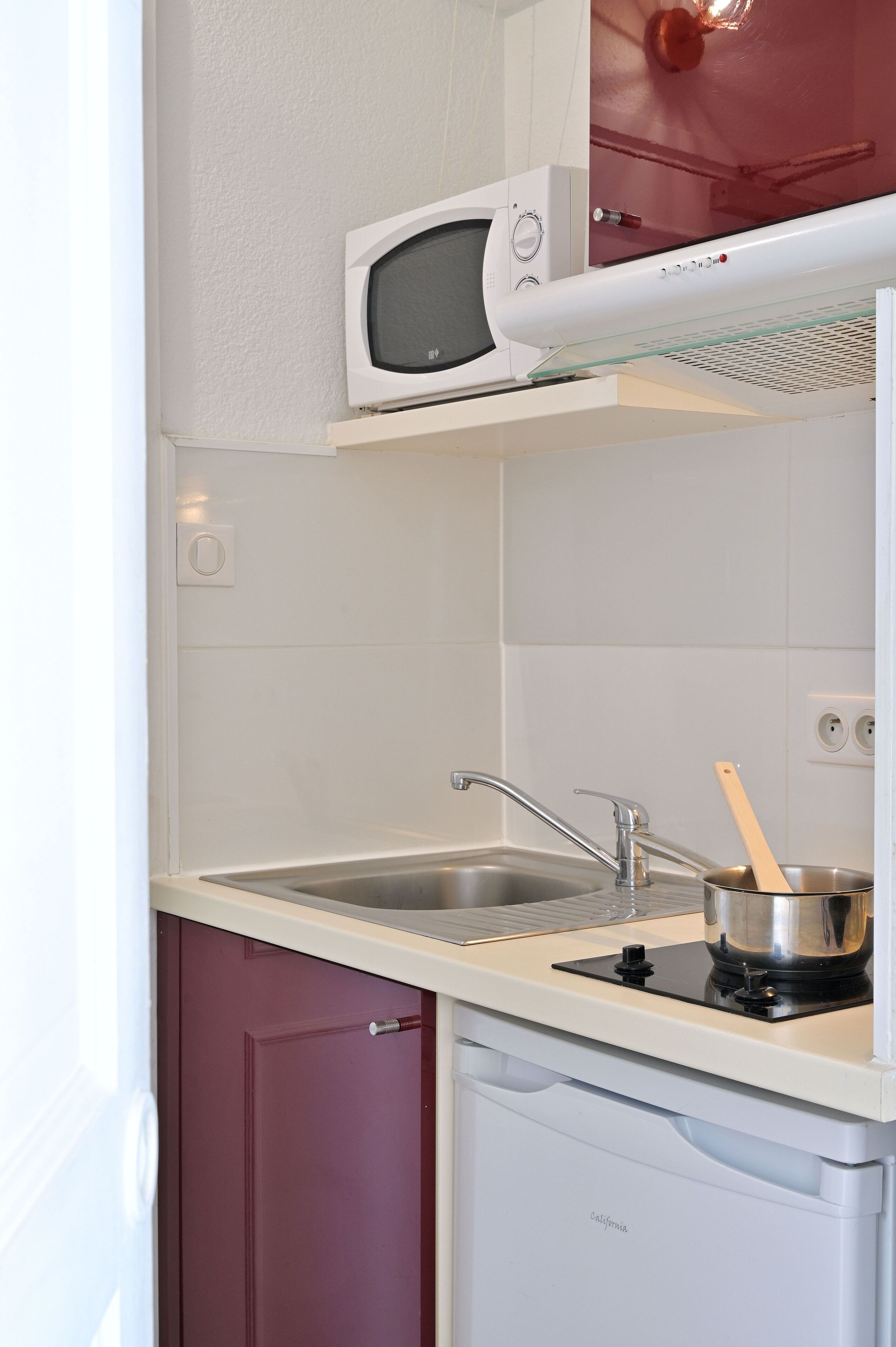 A compact kitchen with a microwave, sink, and a dish drying rack.