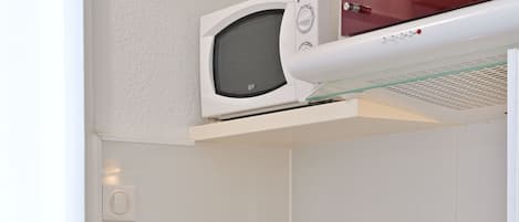 A compact kitchen with a microwave, sink, and a dish drying rack.