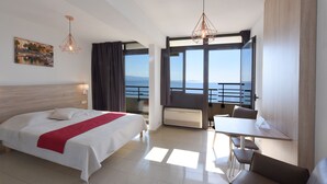 Ein Hotelzimmer mit Bett, Schreibtisch und einem Balkon mit Meerblick.