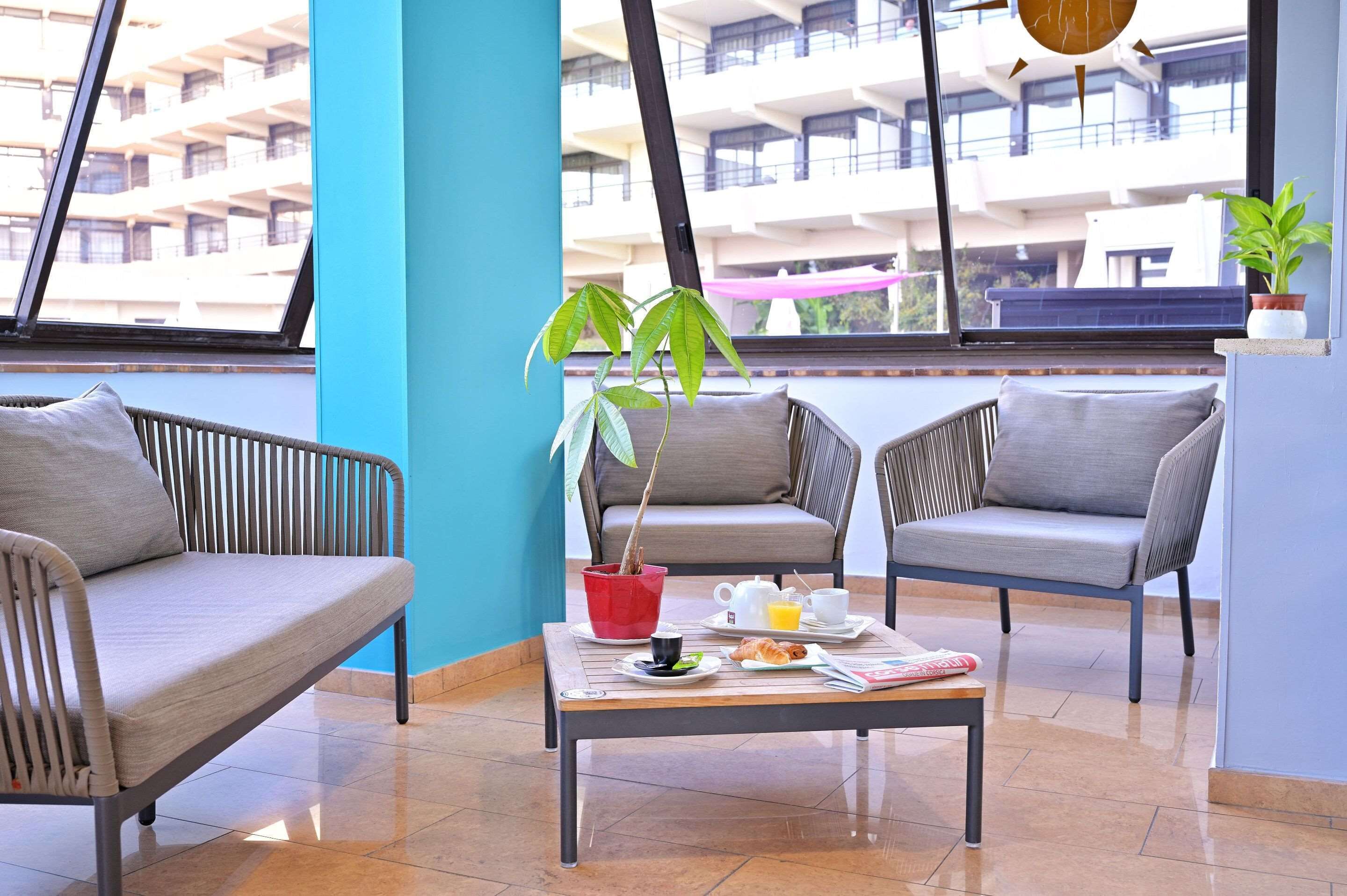 A modern lounge area with two grey sofas, a coffee table with breakfast items, and a potted plant.