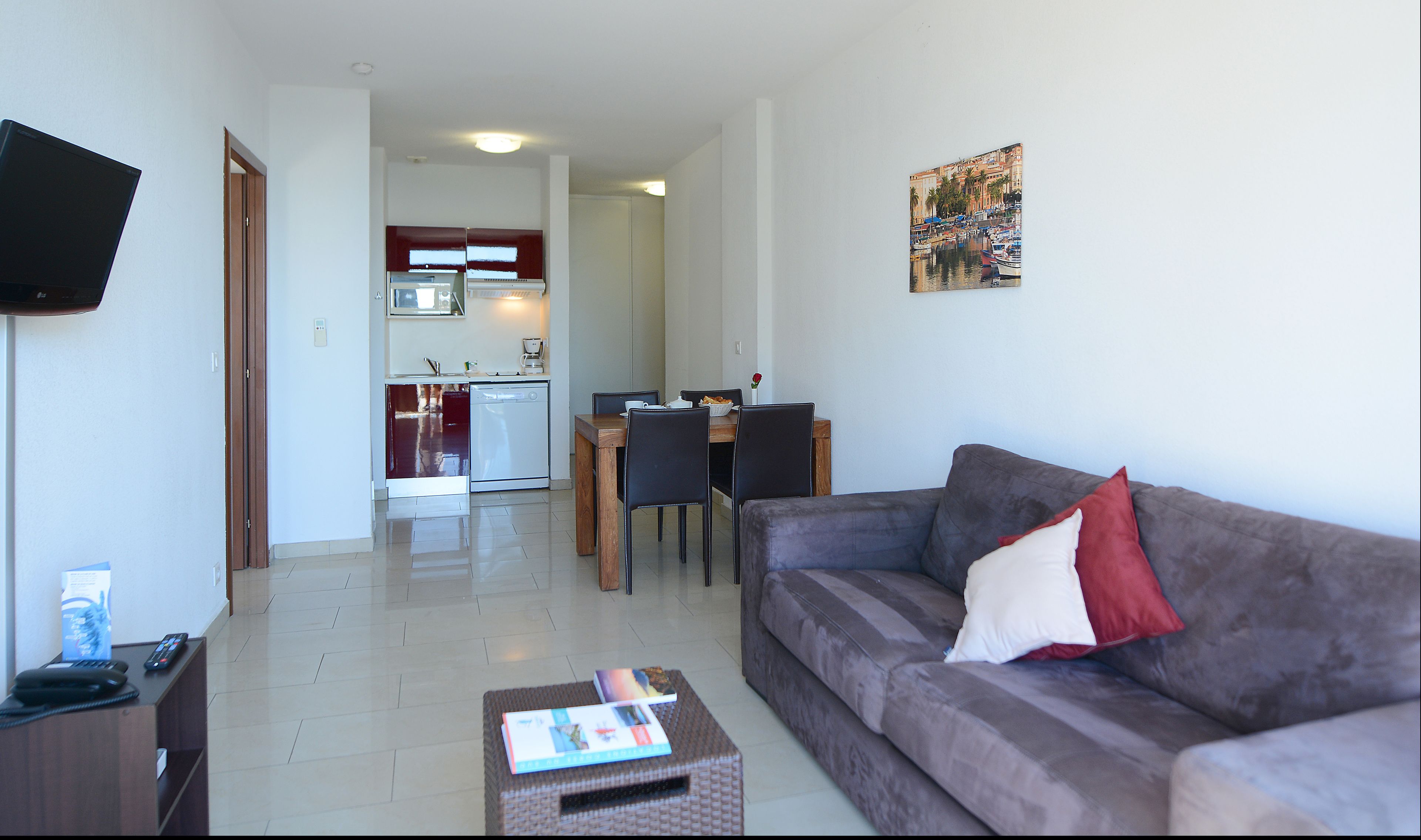 A living room with a sofa, a coffee table, and a TV. There is a dining area with a table and chairs.