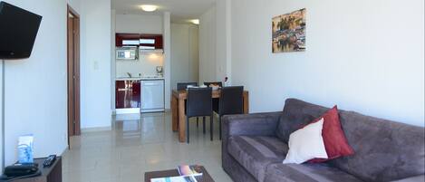 A living room with a sofa, a coffee table, and a TV. There is a dining area with a table and chairs.