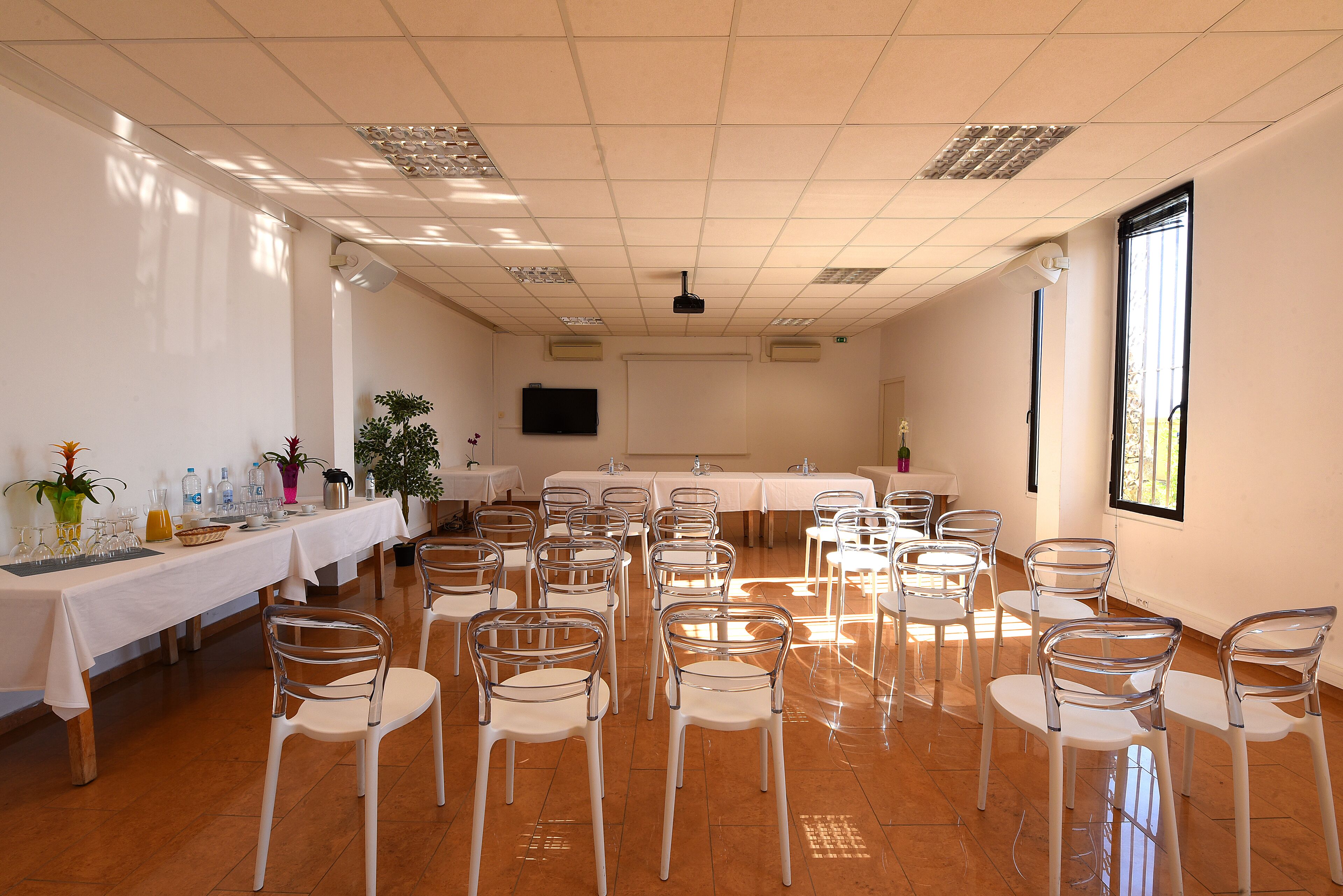 Een vergaderzaal met witte tafels, stoelen en een scherm voor een projecter.