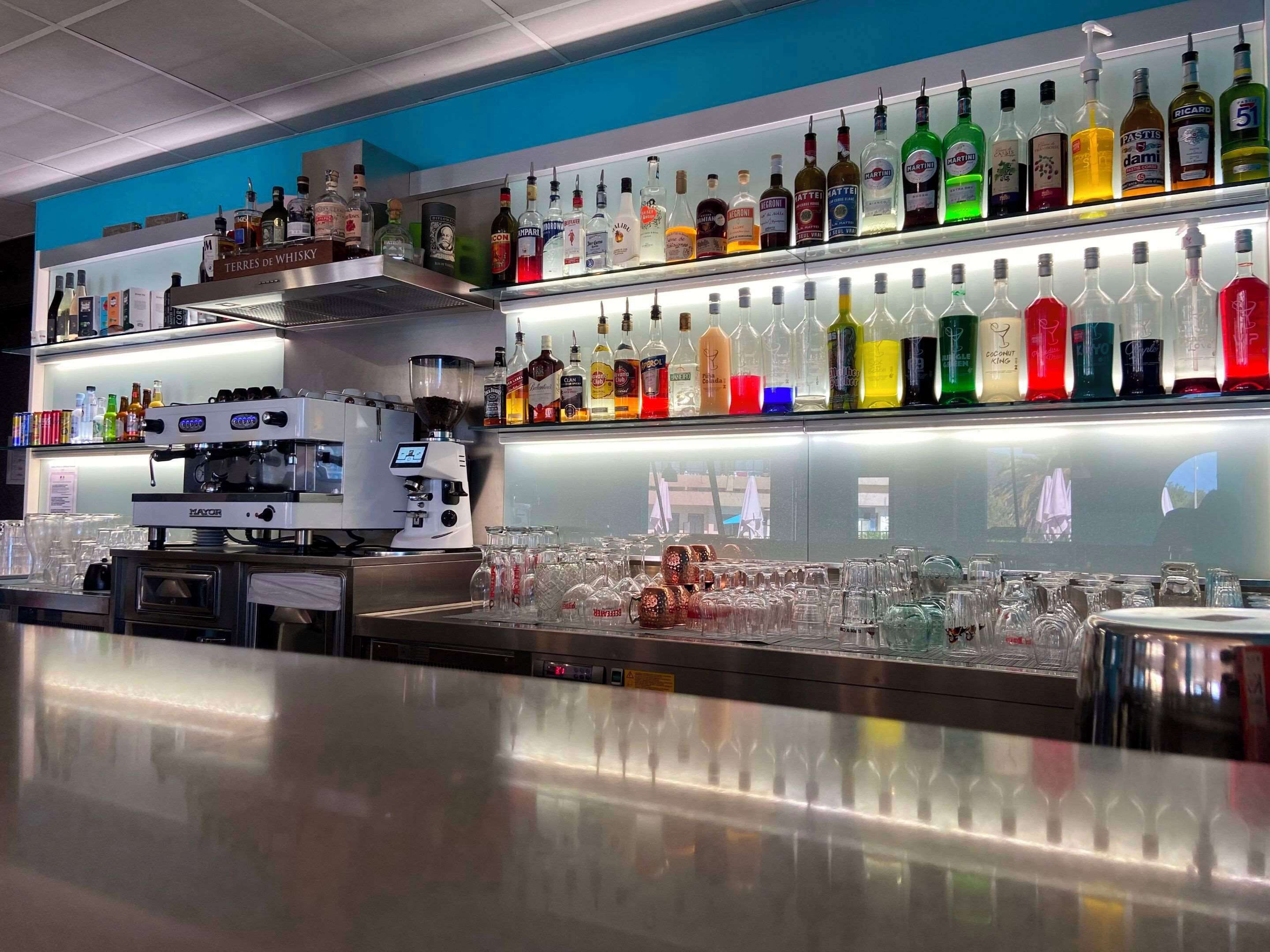 Un espace bar équipé d’une machine à café et de différentes bouteilles d’alcool présentées sur des étagères.