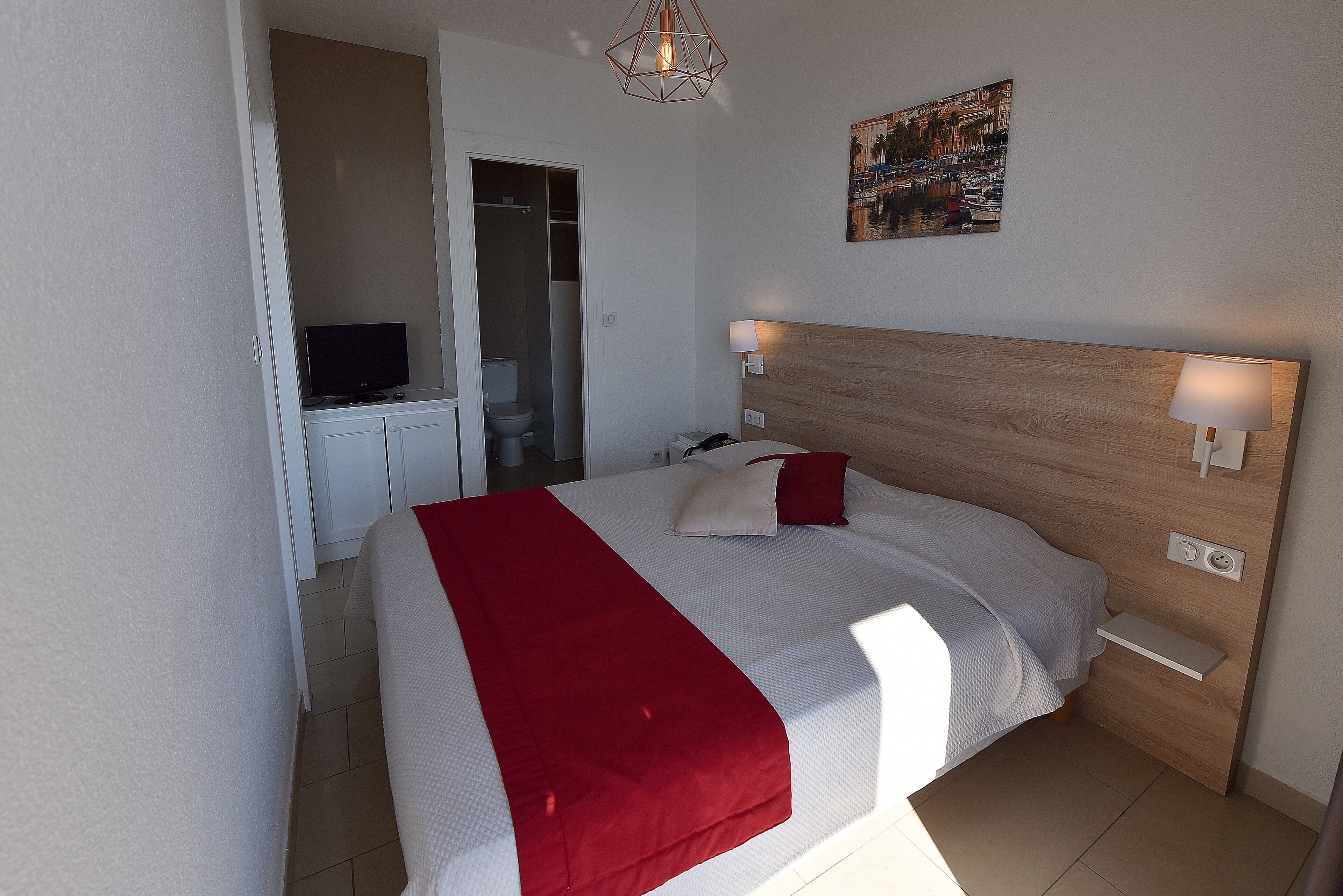 Ein ordentlich eingerichtetes Schlafzimmer mit Bett, Nachttischlampen, einem Fernseher und einem Bild an der Wand.