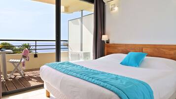 Een slaapkamer met een groot bed, een balkon met uitzicht op zee, en een klein tafeltje met een stoel.