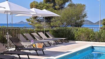 Area piscina con sedie a sdraio e ombrelloni, vista libera sul mare e piscina piastrellata.
