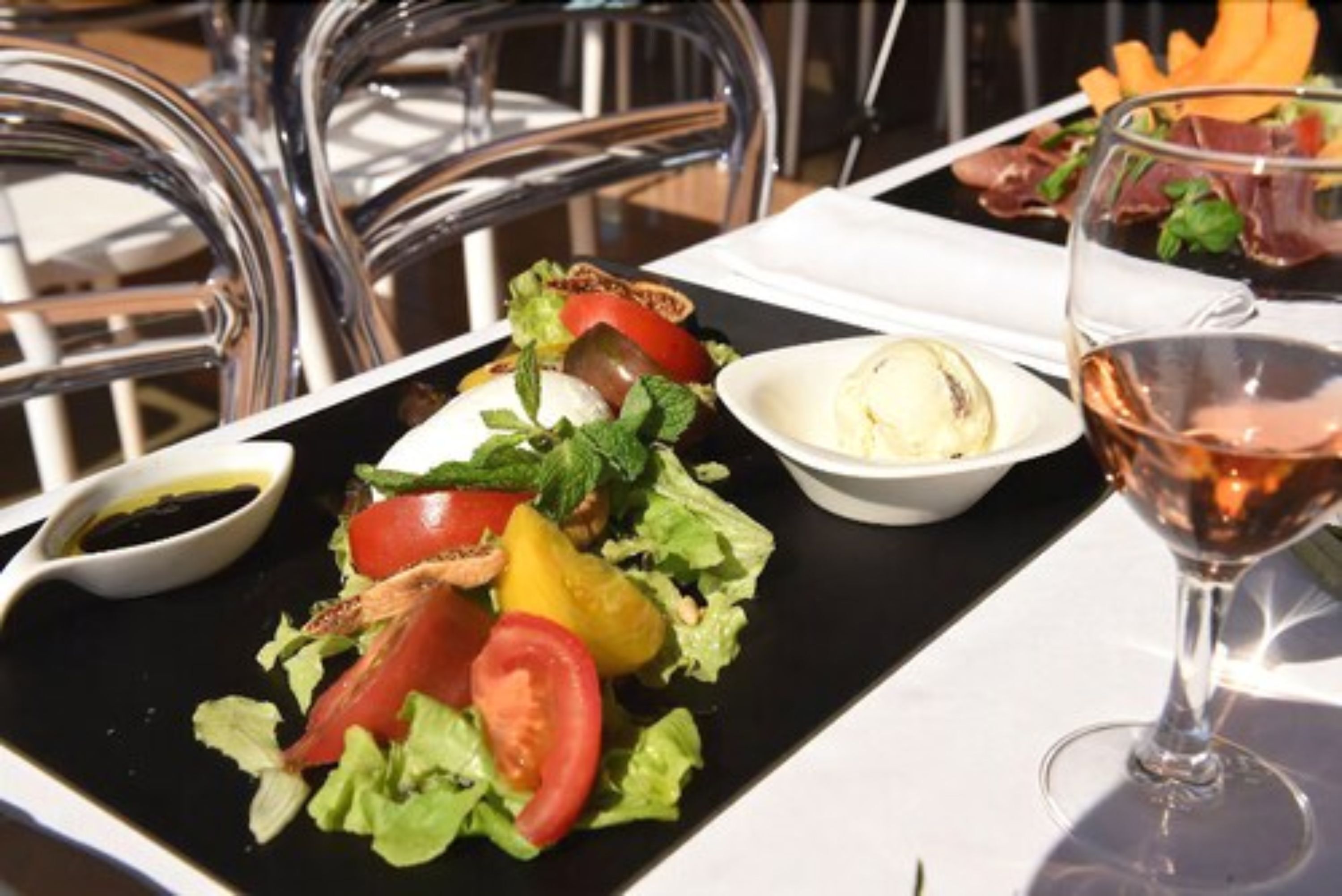 Una mesa con una bandeja negra que contiene una ensalada, un tazón de sopa y una copa de vino.