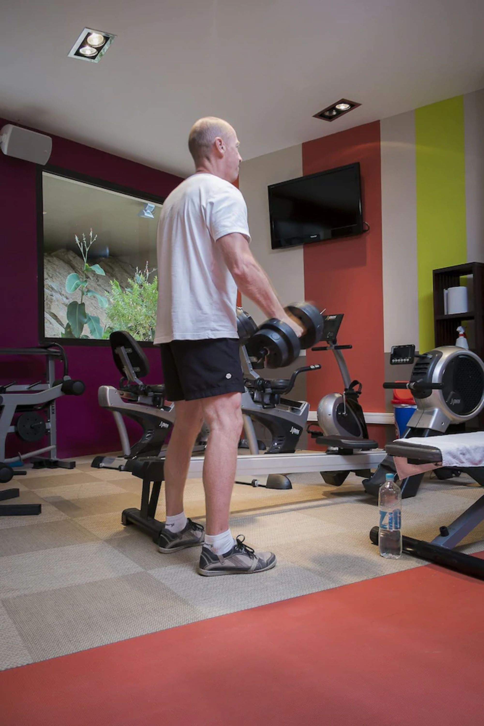A gym with exercise equipment, a television on the wall, and a mirror.