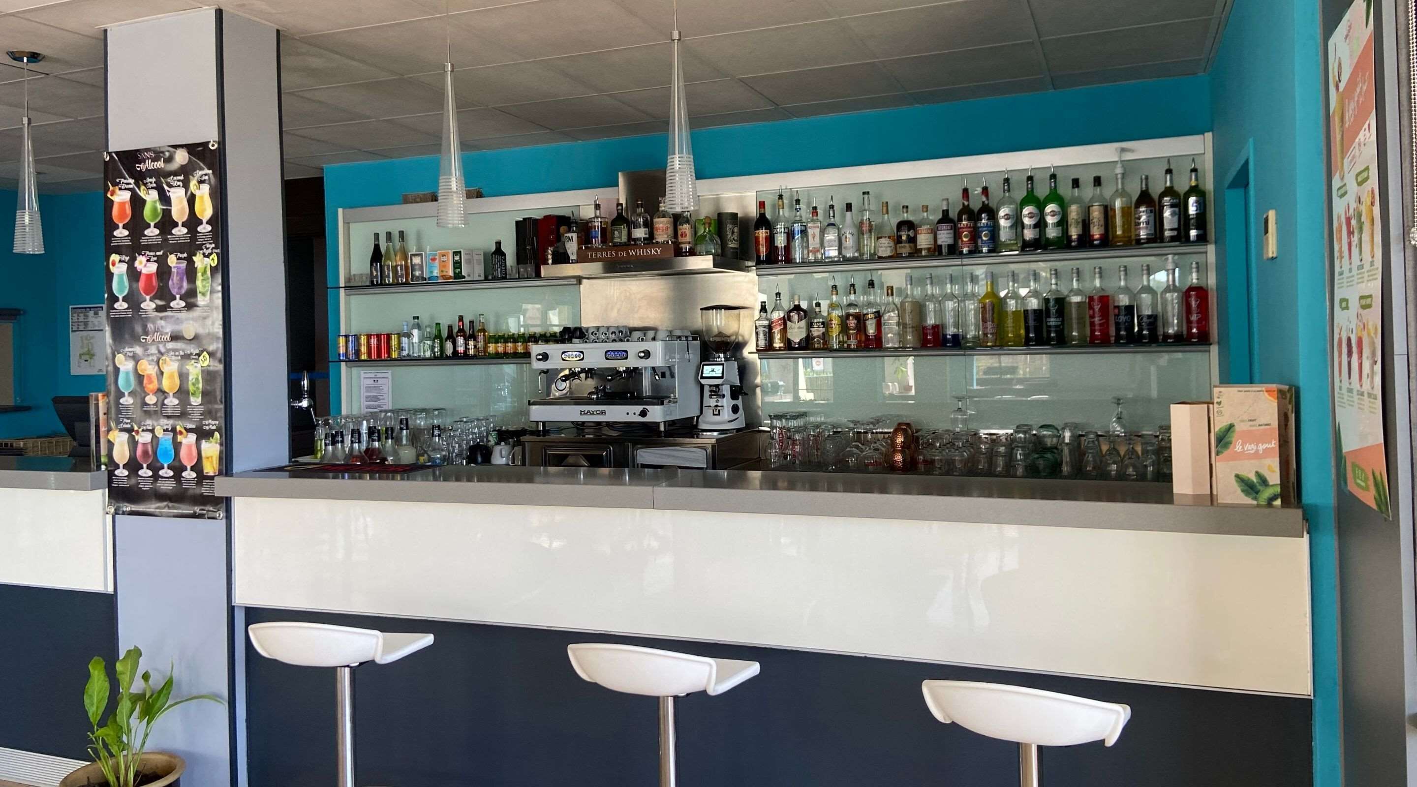 Uma área de bar com uma máquina de café, prateleiras com garrafas de bebidas e banquetas.