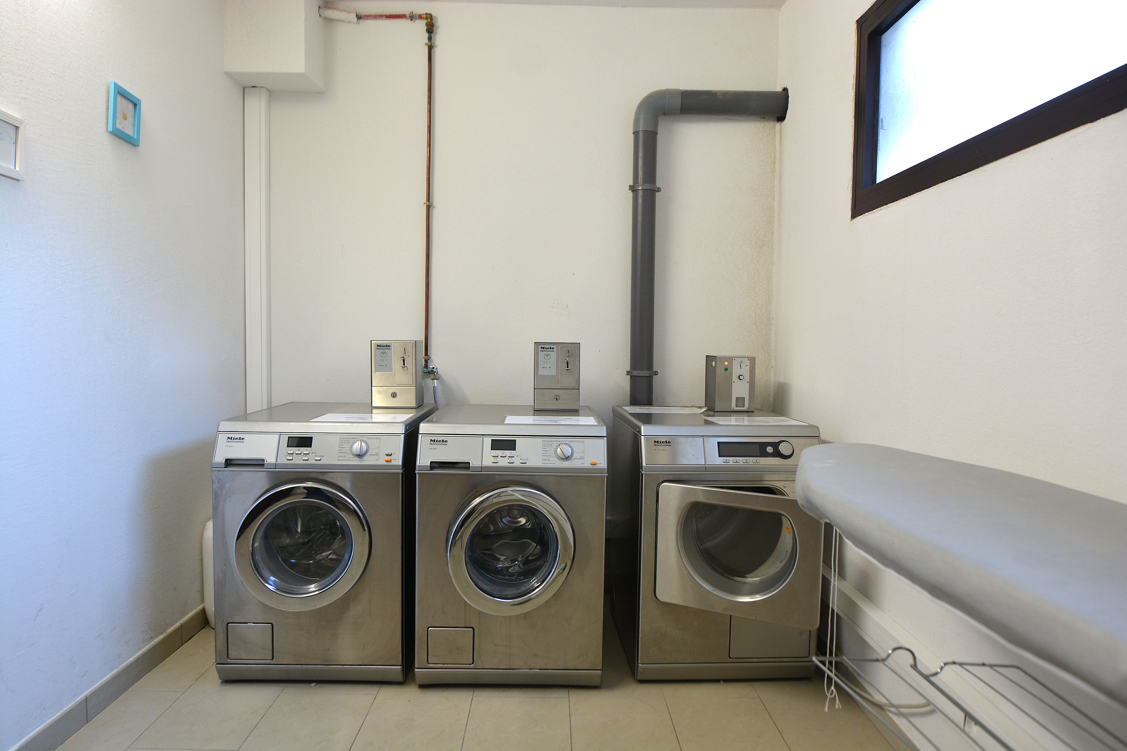 A laundry area with three stacked washing machines, a water heater, and a window.