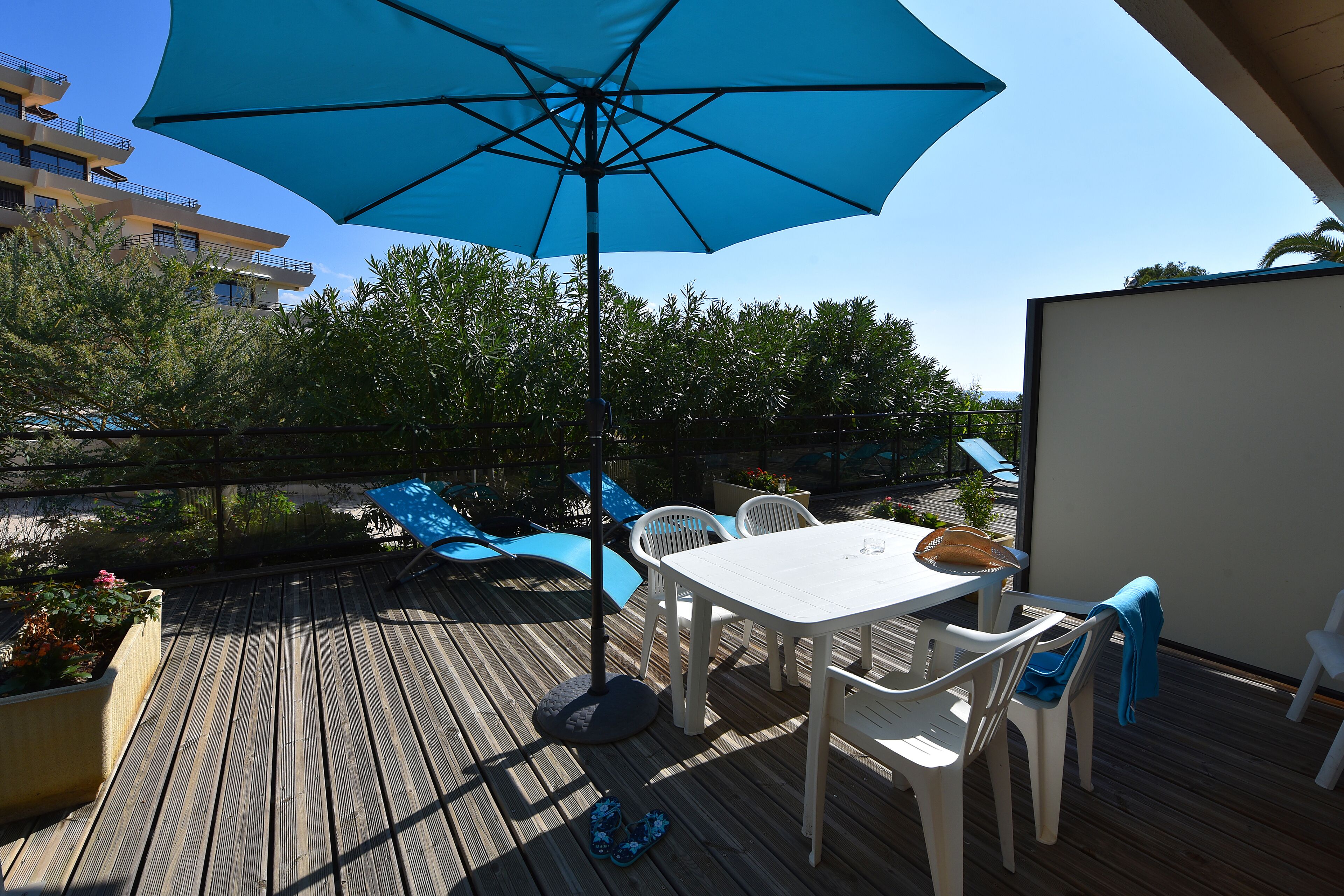 A wooden deck with a table and chairs, a blue umbrella, and a view of a building in the background.