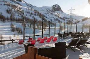 Eine verschneite Berglandschaft mit einer Restaurant-Sitzgelegenheit, inklusive Außenbereich mit Tischen und Stühlen.