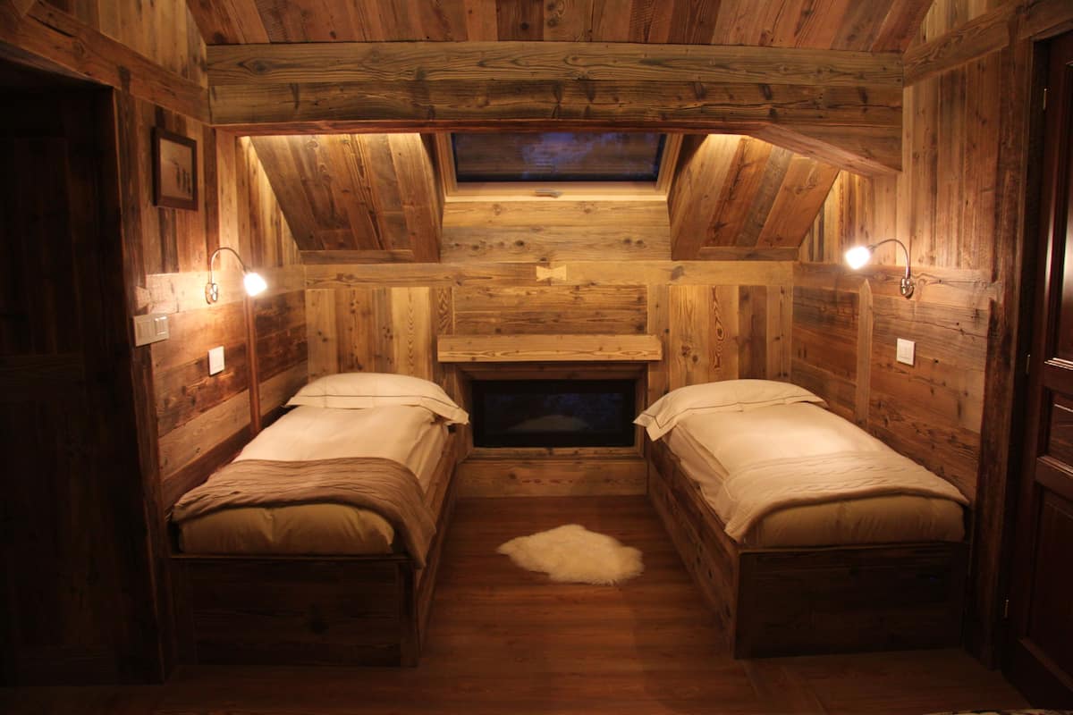 A cabin with two wooden beds, a fur rug, and a skylight.