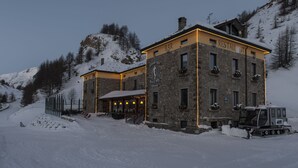 Un edificio de piedra con bar y restaurante en la planta baja, rodeado de colinas cubiertas de nieve.