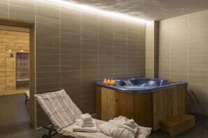 A spa room with a wooden tub, a lounge chair, and a towel stack. - Hotel Maison de Neige (La Thuile)