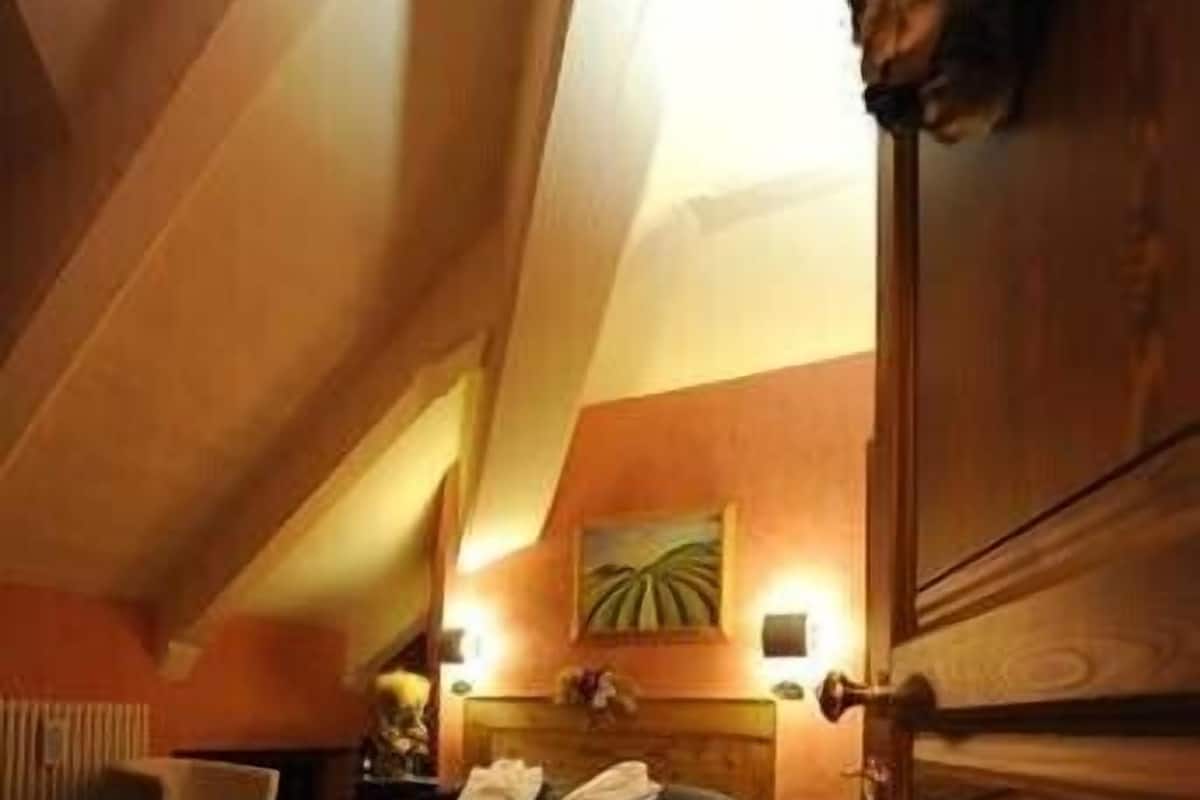 A cozy attic bedroom with a sloped ceiling, a wooden bed, a nightstand, and a wall-mounted lamp.