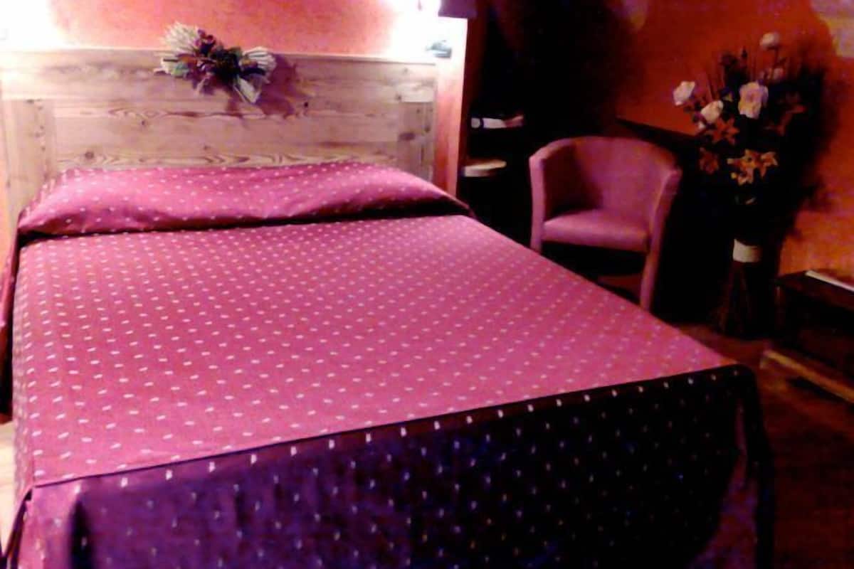 A bed with a pink polka dot bedspread and matching pillows, a wooden headboard, a chair, and a vase with flowers.