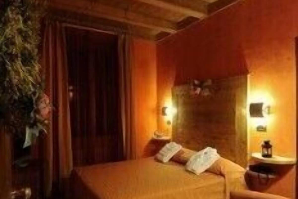 A cozy room with a wooden ceiling, a bed with a headboard, a bedside table, and a chair.