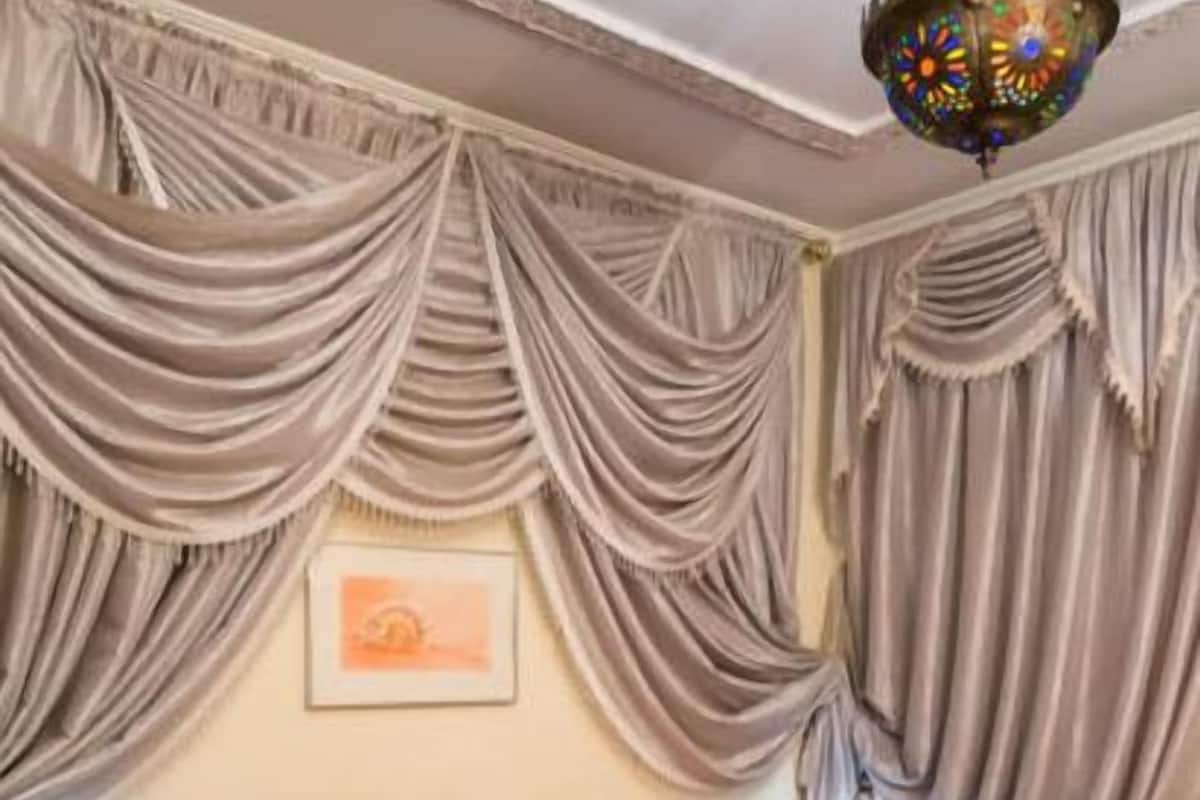 Una habitación de hotel con una cama grande, dos almohadas, una colcha roja, una toalla blanca, un piso a cuadros y un candelabro.